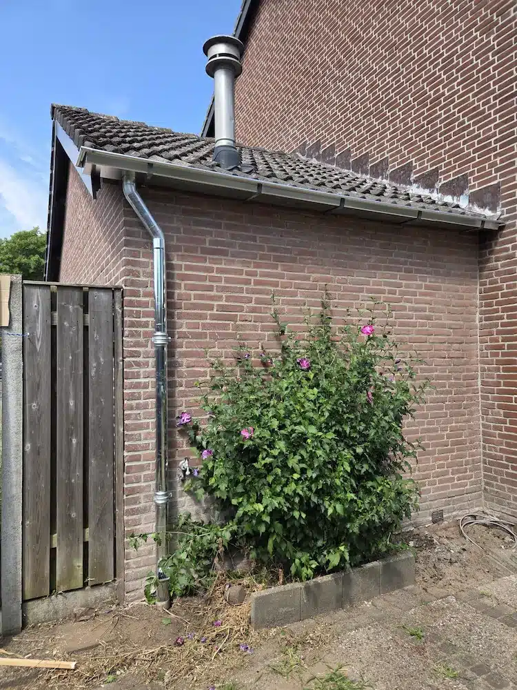 Nieuwe hemelwaterafvoer langs de zijgevel van de woning na vervanging van de dakgoot