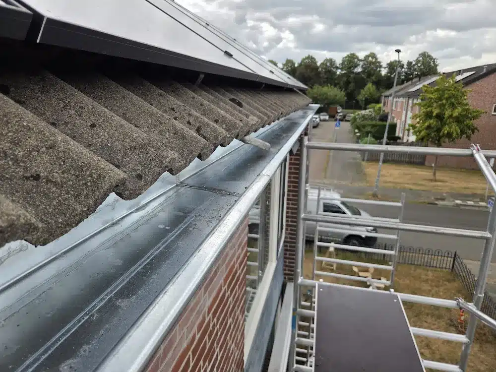 Nieuwe zinken dakgoot langs de dakrand, gezien vanaf de steiger met zonnepanelen op het dak